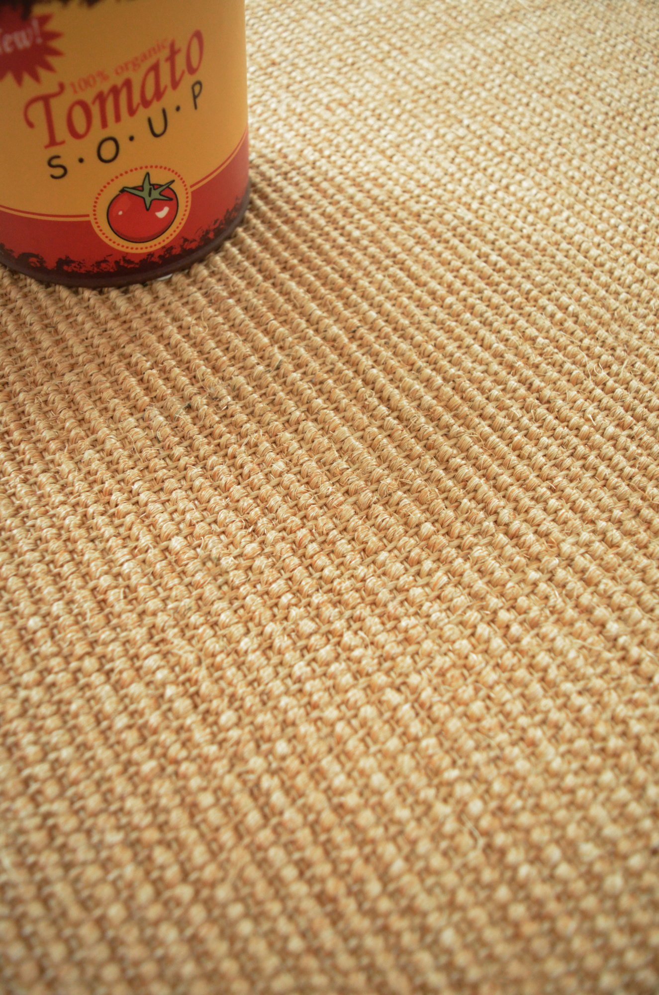 Sol Sisal - Minimal - Camel doré montrant le détail du tissage près d’une bouteille rouge et jaune