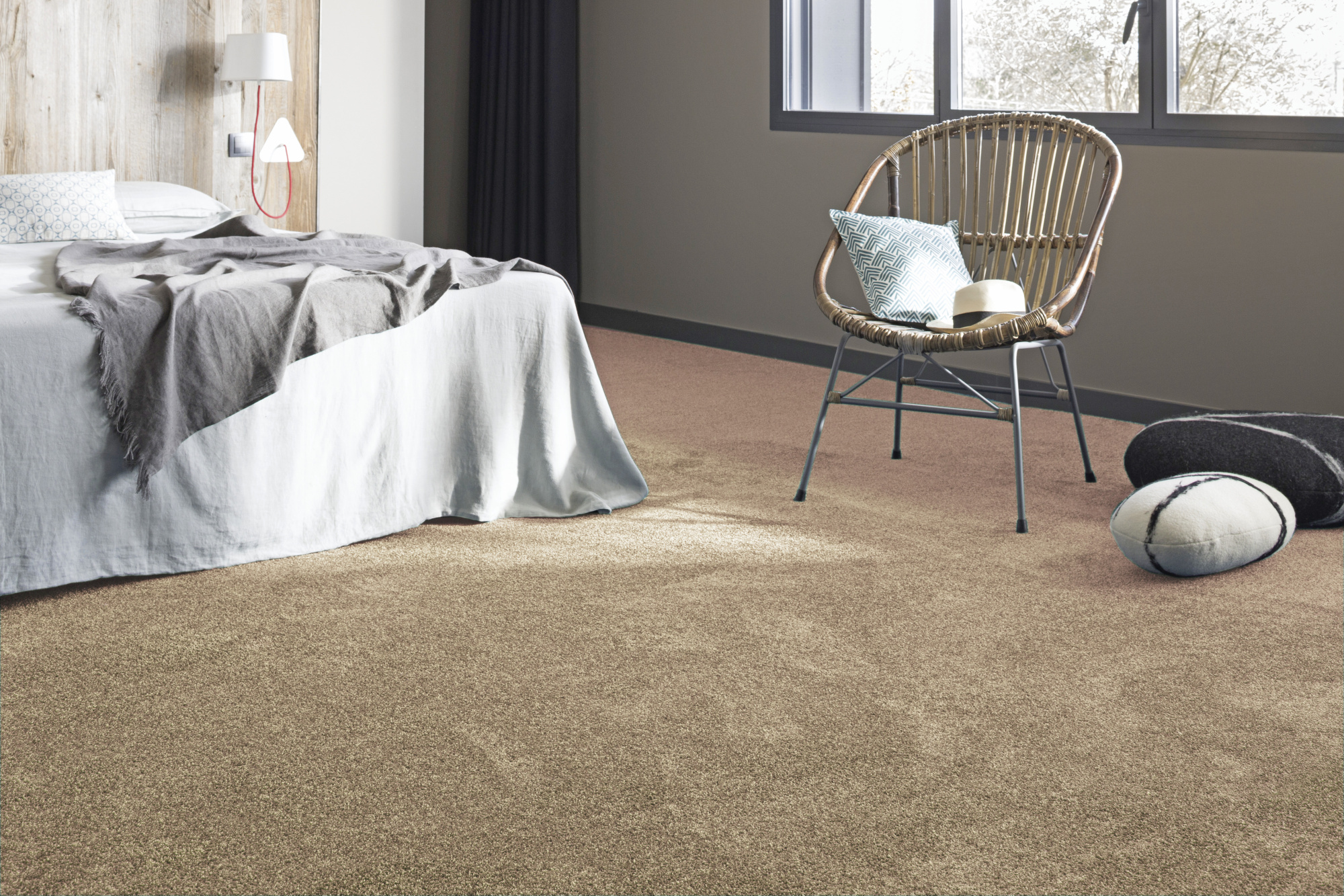 Moquette douce Délicatesse - Beige caramel au pied d'un lit avec fauteuil en rotin et coussins aux tons naturels