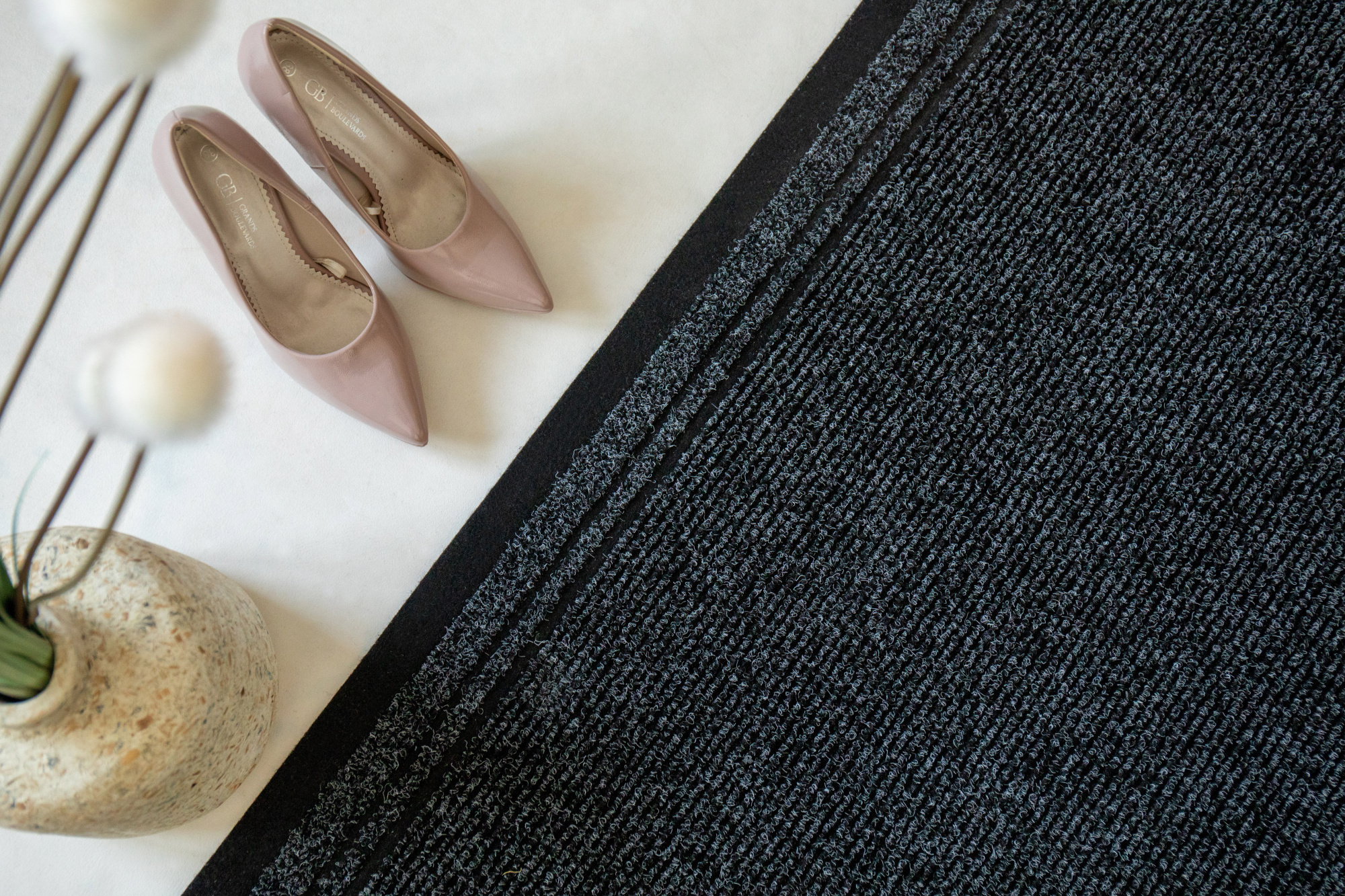 Tapis de passage Antidérapant au mètre - Noir présenté dans une ambiance déco avec chaussures et accessoires