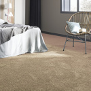 Moquette douce Délicatesse - Beige caramel au pied d'un lit avec fauteuil en rotin et coussins aux tons naturels