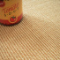 Sol Sisal - Minimal - Camel doré montrant le détail du tissage près d’une bouteille rouge et jaune